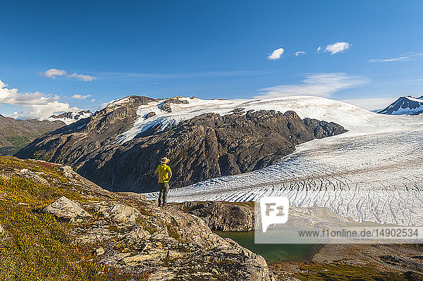 A man hiking near the Harding Icefield Trail with the Kenai Mountains and an unnamed hanging glacier in the background  Kenai Fjords National Park  Kenai Peninsula  South-central Alaska; Alaska  United States of America