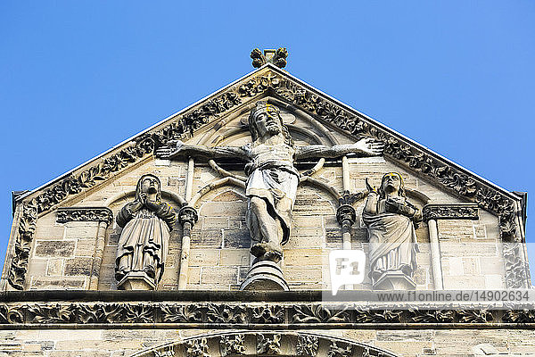 Nahaufnahme eines Kruzifixes auf der Spitze einer steinernen Kirchenfassade mit blauem Himmel; Trier  Deutschland