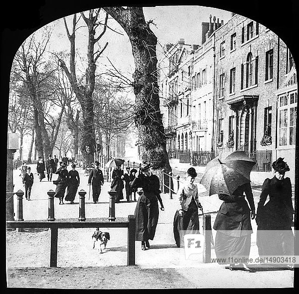 Diapositiv mit Laterna Magica um 1900  viktorianisch/edwardianisch  Sozialgeschichte. Eine typische Londoner Straße mit Menschen  die den Weg entlanggehen. Eine Dame mit aufgespanntem Regenschirm zum Schutz vor der Sonne und einem Hund  der sie begleitet. Gentlemen in Anzügen