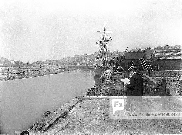 Glasnegativ um 1920. Sozialgeschichte. Blick auf den Fluss mit einem Mann  der Zeitung liest  und einem Segelschiff im Hafen. Whitby Yorkshire