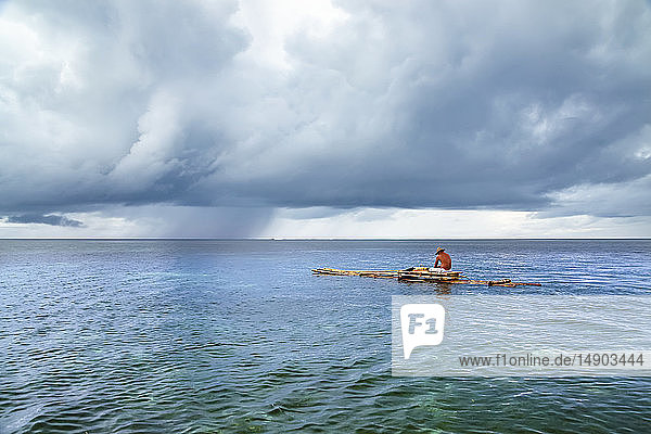 Eine Regenzelle zieht vor der Küste eines Fischers auf einem Bambusfloß vor der Insel Yap vorbei; Yap  Mikronesien