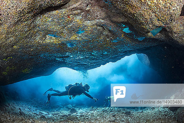 Divers inside a shallow tide pool canyon area off the backside of Lanai near Kaumalapau Harbor Hawaii. Aerated surf materializes as clouds when waves pour into the area and pockets of exhaled air appear as reflective mercury on the ceiling; Lanai Hawaii United States of America