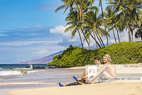 A couple with snorkel gear on a beach with palm trees; Maui  Hawaii  United States of America