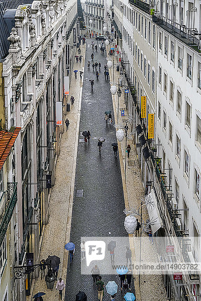Pedestrians with umbrellas walk the narrow street in between buildings; Lisbon  Lisboa Region  Portugal