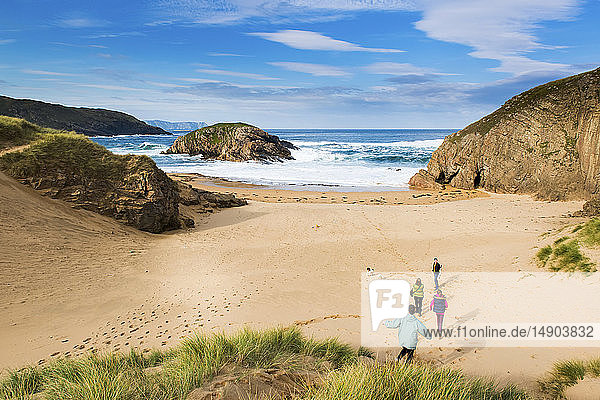 Eine Familie läuft mit ihrem Hund über den Sand und genießt den Strand an der irischen Küste; Irland