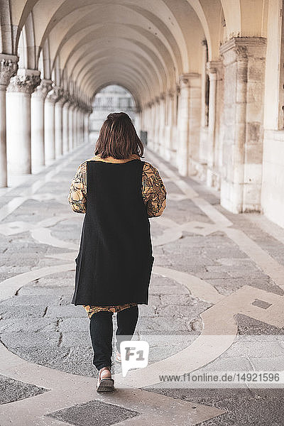 Rückansicht einer Frau  die an einer Kolonnade in Venedig  Venetien  Italien  entlanggeht.