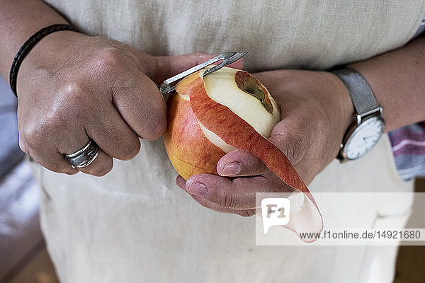 Close up of person peeling a red apple with a double bladed peeler.