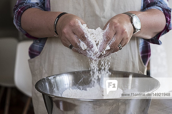 Close up of person wearing apron standing in kitchen  mixing ingredients for a crumble in metal bowl.