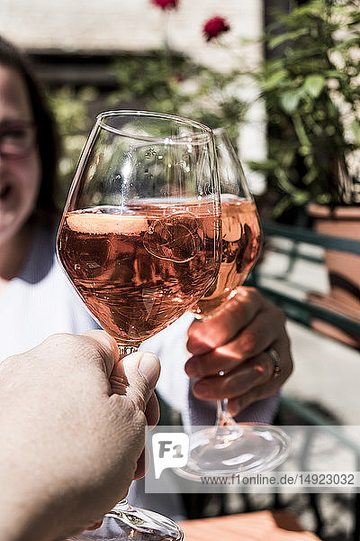 Woman and another person sitting at a table toasting with wine glasses of Aperol Spritz.