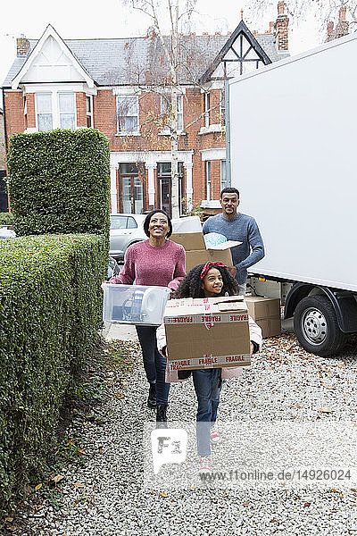 Eine Familie zieht in ein neues Haus ein und trägt ihre Habseligkeiten aus dem Umzugswagen in die Einfahrt