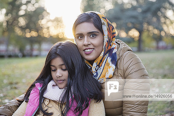 Portrait smiling mother in hijab sitting in autumn park with daughter