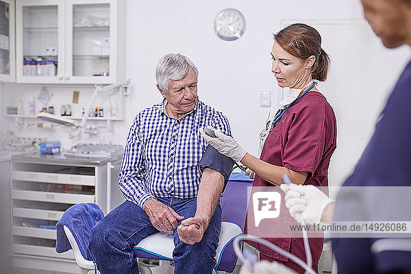 Arzt kontrolliert den Blutdruck eines älteren Patienten im Untersuchungsraum einer Klinik