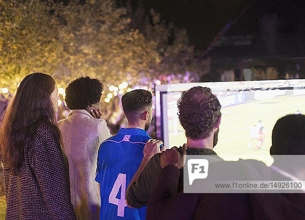Freunde sehen sich ein Fußballspiel auf einer Projektionsfläche im Hinterhof an