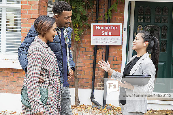 Immobilienmakler im Gespräch mit einem Paar vor einem zu verkaufenden Haus
