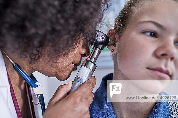 Close up female pediatrician using otoscope  examining ear of girl patient