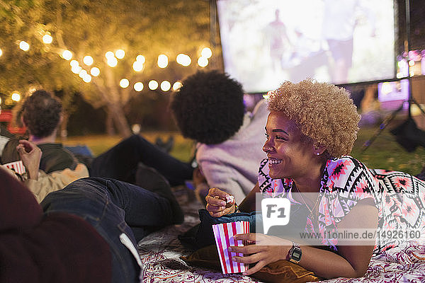 Glückliche Frau  die Popcorn isst und mit Freunden im Hinterhof einen Film schaut