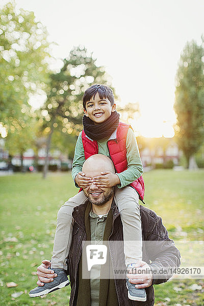 Portrait playful son riding on fathers shoulders in autumn park