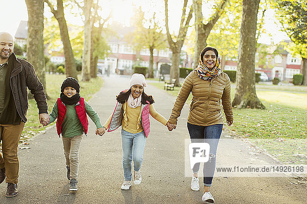 Glückliche muslimische Familie  die sich an den Händen hält und im Herbst im Park spazieren geht
