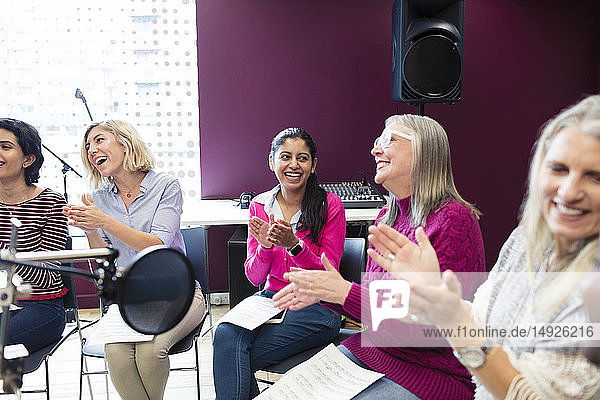 Happy womens choir with sheet music singing and clapping in music recording studio