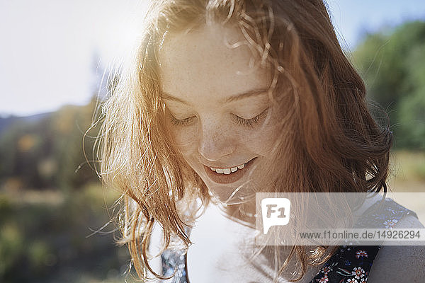 Lächelnde junge Frau mit Sommersprossen blickt nach unten