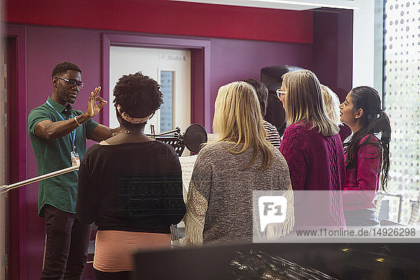 Male conductor leading women singing in music recording studio