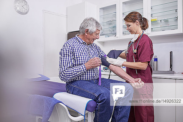 Female nurse checking blood pressure of senior male patient in clinic examination room