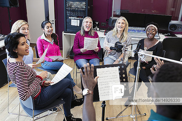 Male conductor leading womens choir with sheet music singing in music recording studio
