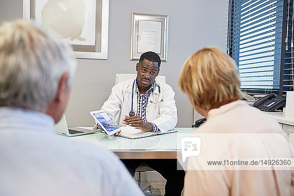 Doctor with digital tablet talking to senior couple in clinic doctors office