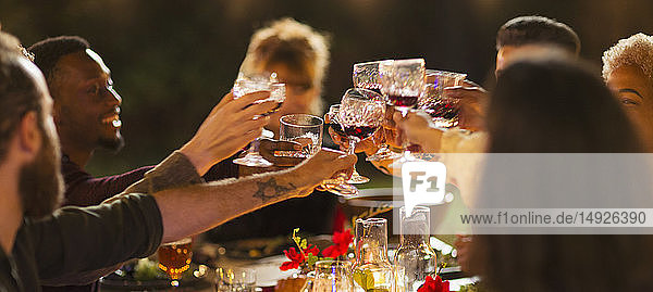 Freunde stoßen mit Weingläsern an und genießen das Abendessen auf einer Gartenparty