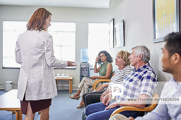 Female doctor talking with patients waiting in clinic waiting room