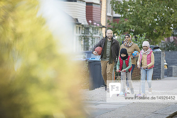 Muslim family walking and riding scooters on neighborhood sidewalk