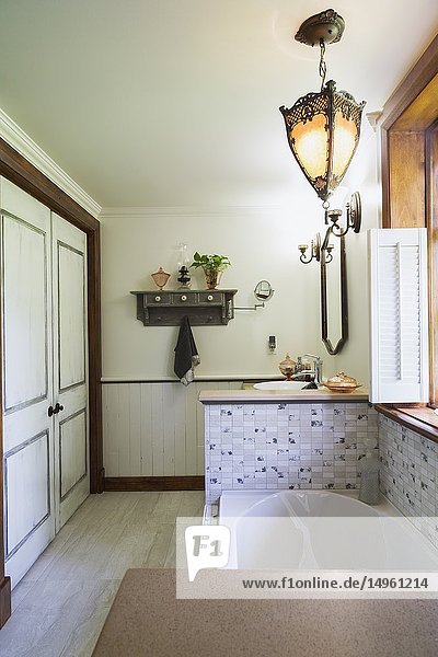 Main bathroom with bathtub encased in ceramic base and medieval style pendent lighting fixture inside an old 1892 Canadiana cottage style home