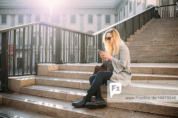 Junge Frau sitzt auf einer Stadttreppe und schaut auf ein Smartphone  Mailand  Italien