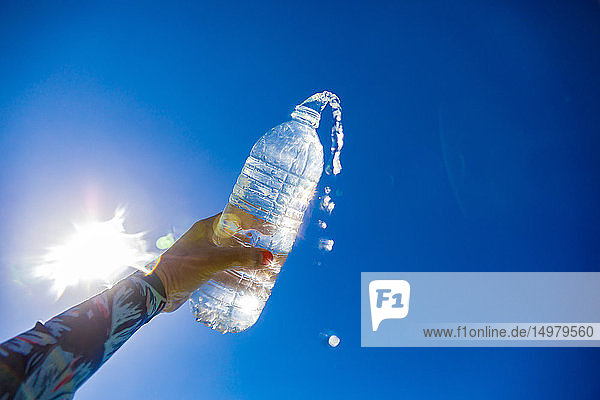 Frau hält Wasserflasche gegen die Sonne