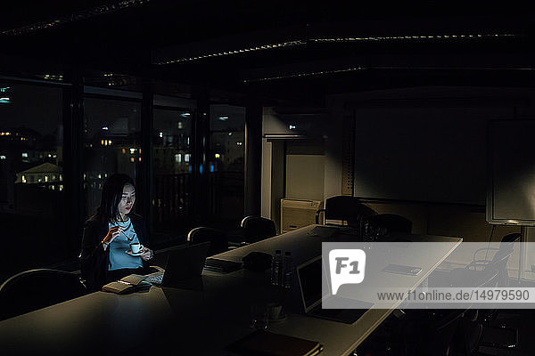 Junge Geschäftsfrau  die nachts im Büro sitzt und auf ihren Laptop schaut