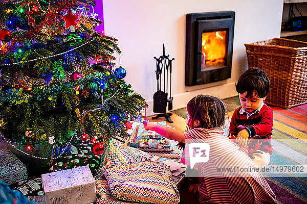 Mädchen und männliches Kleinkind spielen am Wohnzimmer-Weihnachtsbaum