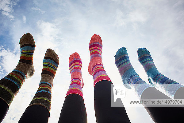 Drei junge Frauen in gestreiften Socken mit gegen den sonnenbeschienenen Himmel erhobenen Beinen  Schrägansicht der Beine