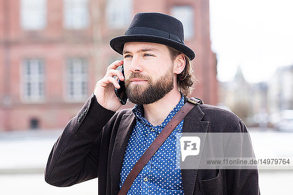 Mann in Trilby macht Smartphone-Anruf auf Stadtstraße