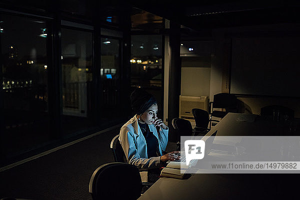 Junge Geschäftsfrau  die nachts im Büro am Laptop tippt