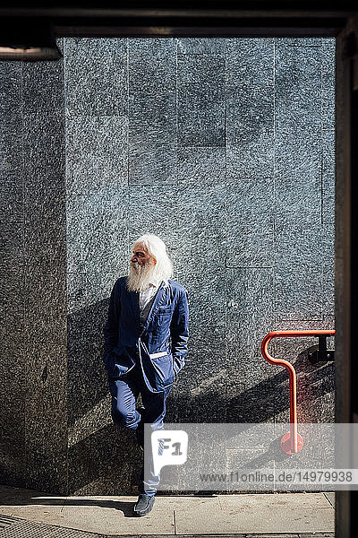 Senior businessman leaning against building wall