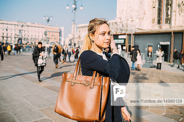 Young female tourist strolling and listening to earphones in city square  Milan  Italy