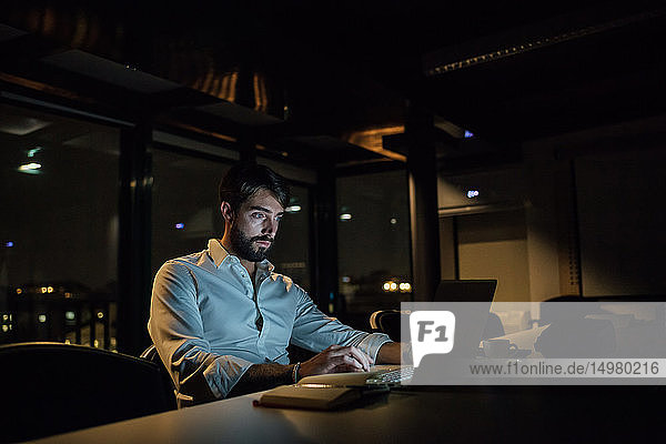 Mittelgroßer erwachsener Geschäftsmann nachts im Büro beim Tippen am Laptop