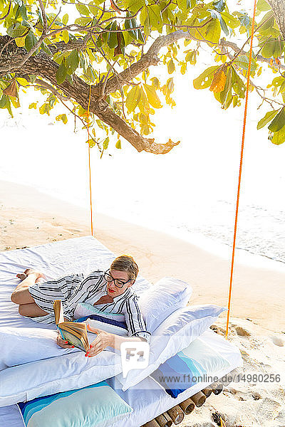 Frau liest Buch auf Schaukelbett am Strand  Insel Ginto  Linapacan  Philippinen