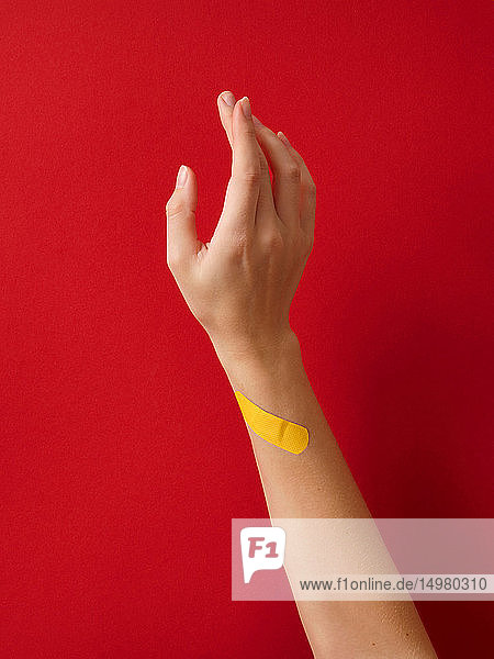 Erste-Hilfe-Klebepflaster am Handgelenk der Frau vor rotem Hintergrund