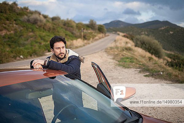 Mann ruht sich am Straßenrand am Auto aus und genießt die Aussicht auf den Hügel  Villasimius  Sardinien  Italien