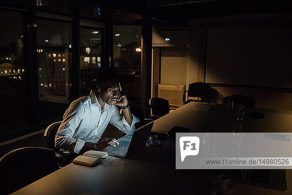 Müde junger Geschäftsmann nachts im Büro beim Tippen am Laptop