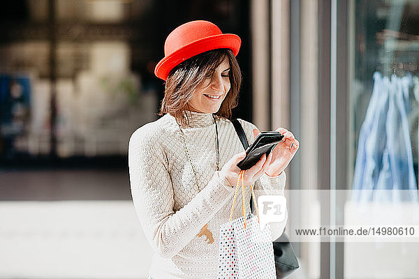 Weibliche Käuferin mit Smartphone vor dem Geschäft