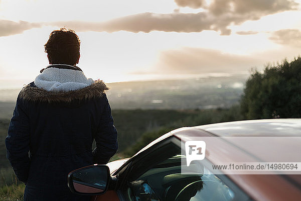 Man resting against car on roadside enjoying view on hilltop
