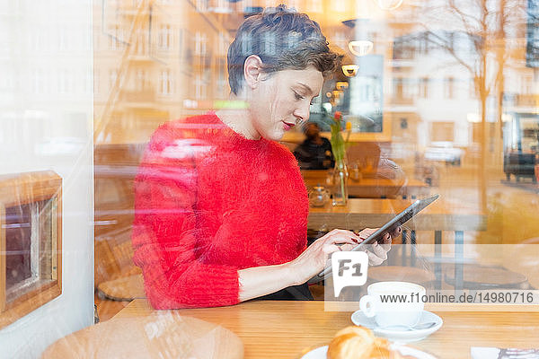 Mittlere erwachsene Frau im Café mit digitalem Tablet-Touchscreen  Fensteransicht