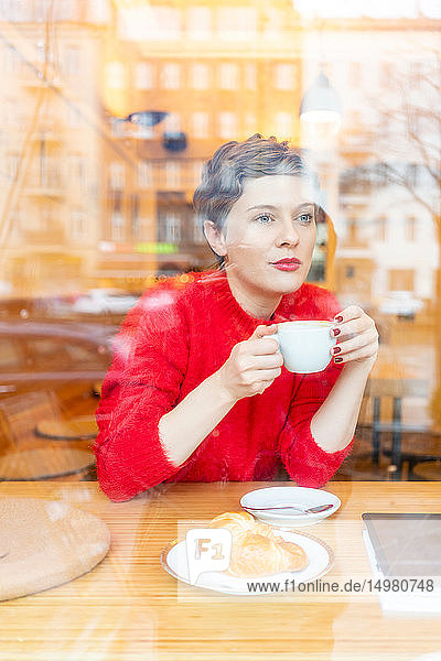 Mittelgroße erwachsene Frau im Café  die Kaffee trinkt und aus dem Fenster schaut